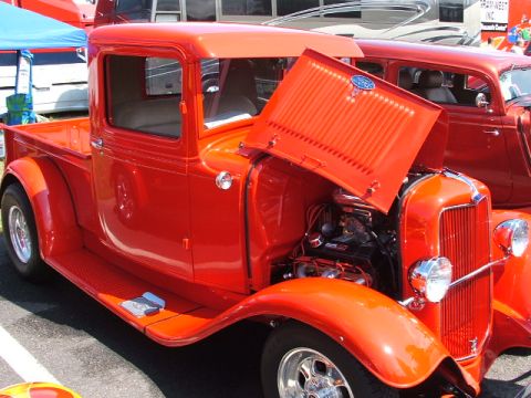 1966 Ford Ranchero - A bright red pickup truck is parked with its hood open, revealing the engine. A second red vehicle is partially visible in the background.