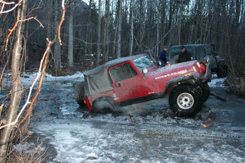 1995 Jeep Cherokee - A red Jeep Wrangler is stuck in icy mud, with another vehicle visible in the background.
