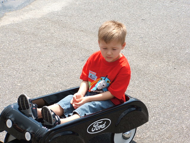 Kid sitting in a black wagon with a Ford logo. He's wearing a red shirt with Thomas the Tank Engine
