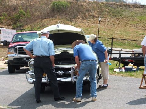 1966 Ford Ranchero - Three individuals inspect the engine of a vintage car, with a red truck visible in the background.