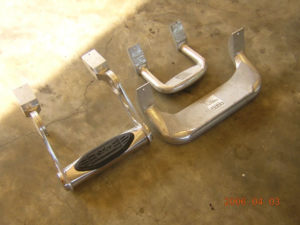 Two polished aluminum truck side step bars with rubber pads lying on a concrete floor