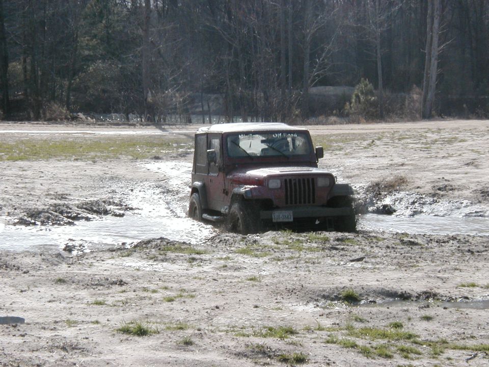 Muddy dark red Jeep Wrangler YJ driving through water hole at off-road park