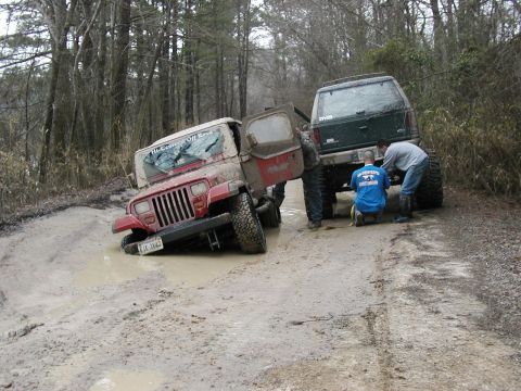 2004 Dodge 2500 - Two off-road vehicles are stuck in the mud on a dirt road, with people attempting to free one of them.