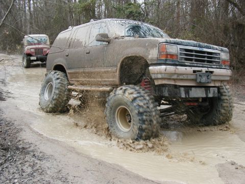 2004 Dodge 2500 - A heavily modified 1995 Ford Explorer navigates a muddy trail, with another off-road vehicle visible behind it.