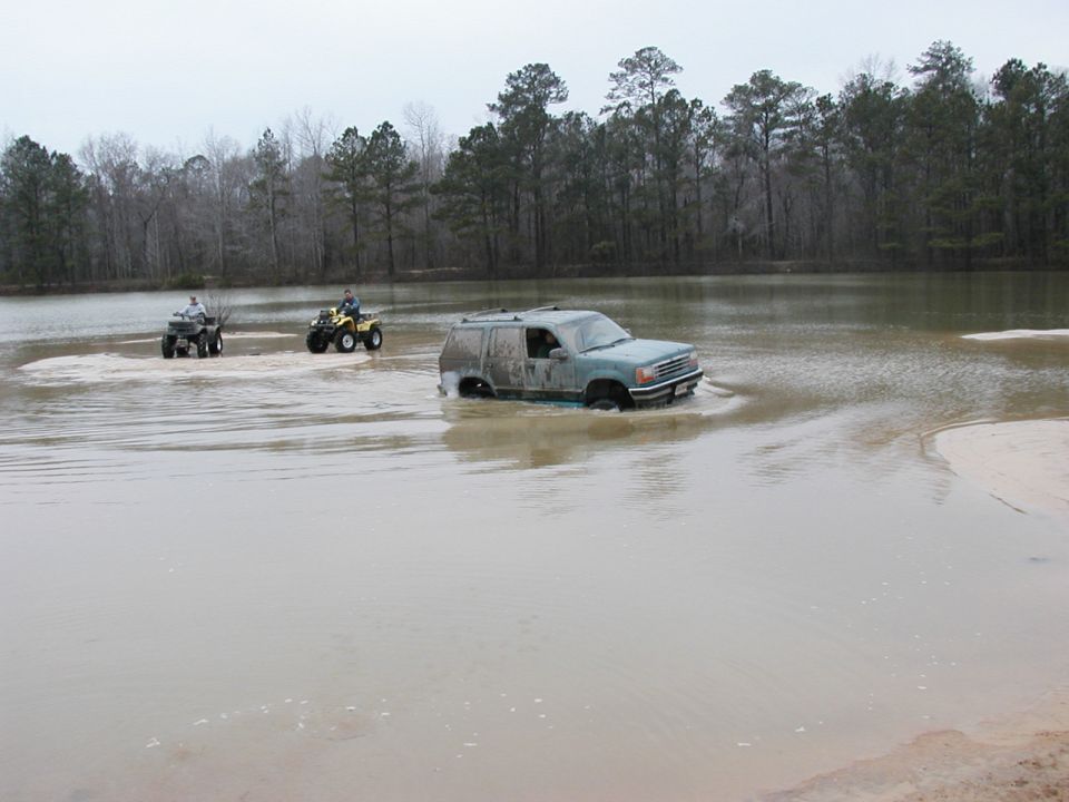 SUV stuck in water with two ATVs nearby