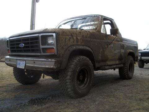 1986 Ford Bronco - This 1986 Ford Bronco is heavily covered in mud, obscuring much of its bodywork but the grille and front end are identifiable. Another vehi…