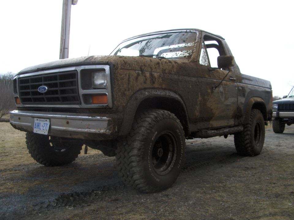 1986 Ford Bronco covered in mud, front 3/4 view. License plate visible