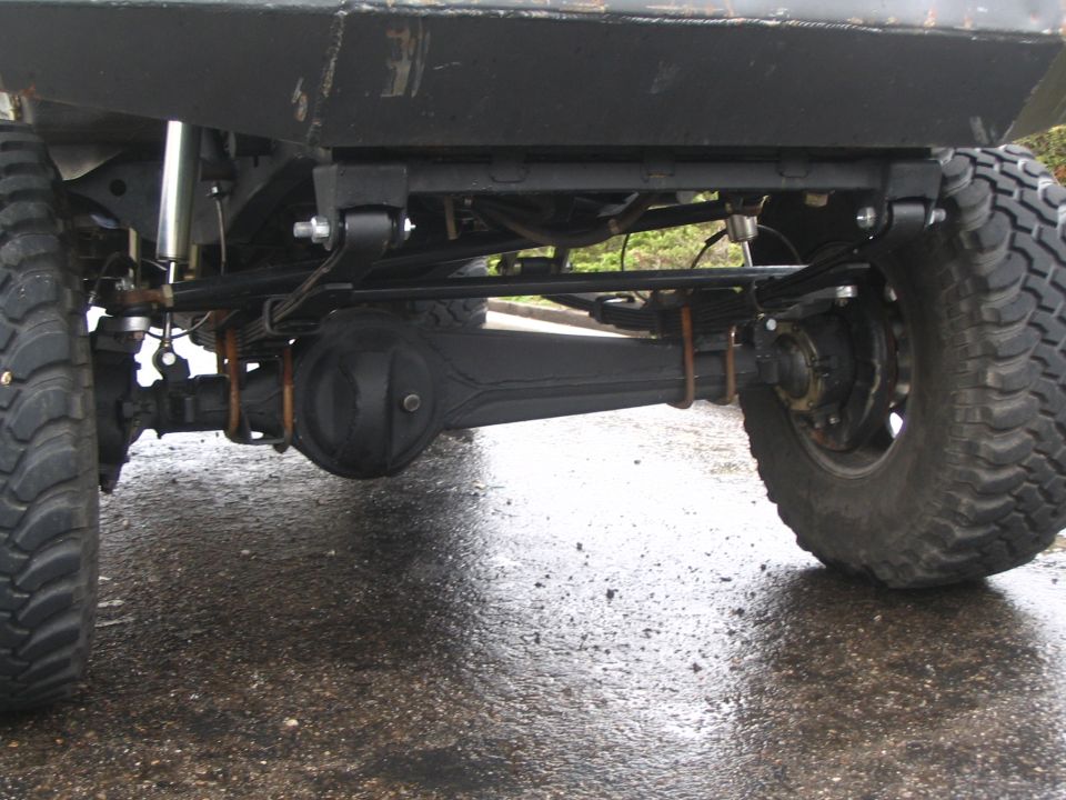 Rear view under a lifted truck showing solid axle, mud tires and exhaust on wet pavement