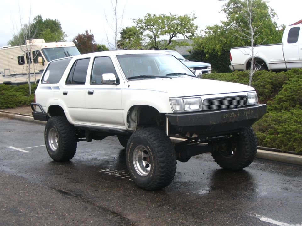White lifted Toyota 4Runner on big mud tires in a parking lot