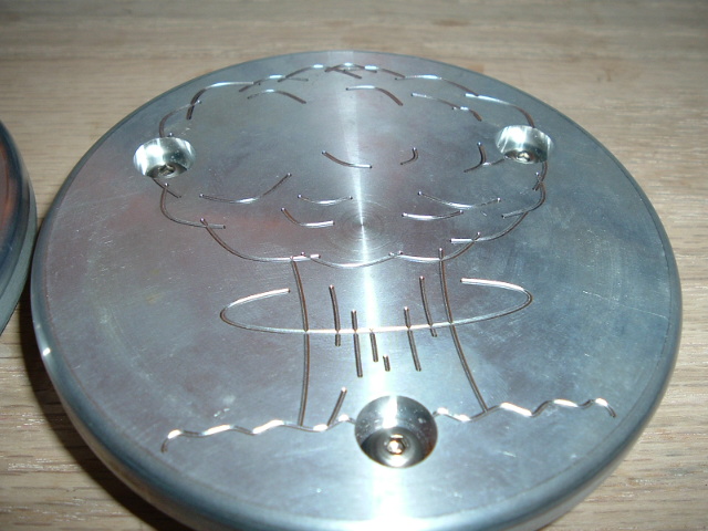 Polished round metal plate engraved with a mushroom-cloud design, three screws