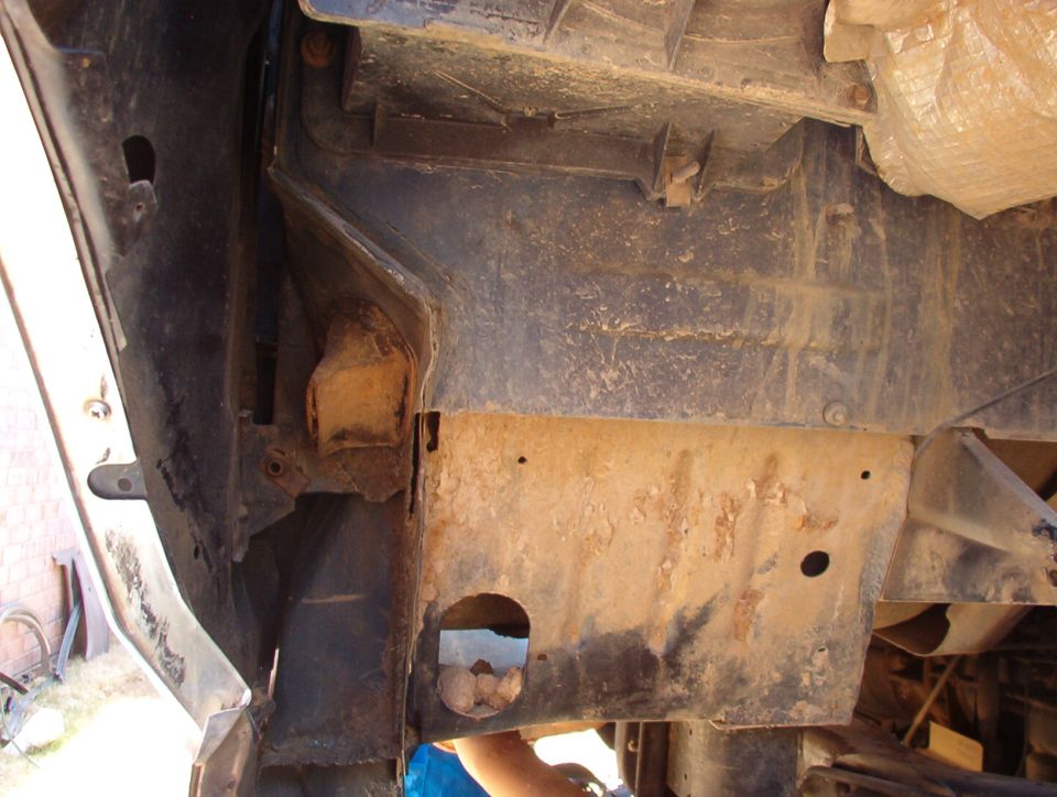 Underside of a vehicle showing rusty crossmember, skid plate and floor pan