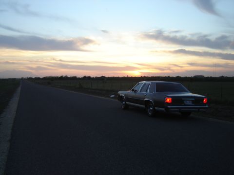 1988 Ford Crown Victoria LTD - A sedan sits on a lonely road as the sun sets, casting a warm glow across the sky.
