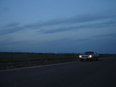 1988 Ford Crown Victoria LTD - A 1988 Ford Crown Victoria LTD is seen from a 3/4 front angle on a rural road as twilight settles.