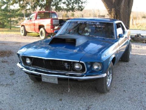 1969 Ford Mustang - A blue 1969 Ford Mustang is parked outside, with a red pickup truck in the background.