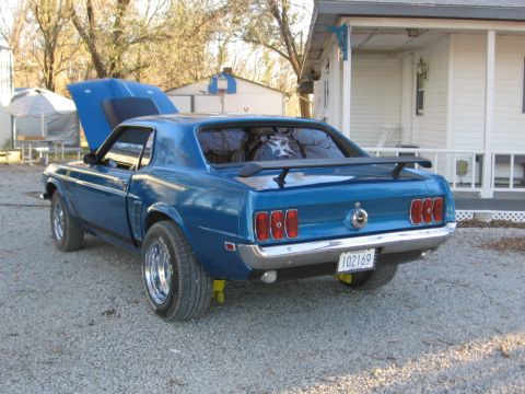 1969 Ford Mustang - Rear view of a blue 1969 Ford Mustang, showing its spoiler and custom wheels, with the hood popped open.