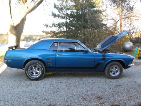 1969 Ford Mustang - Side view of a blue 1969 Ford Mustang coupe, black racing stripes and a spoiler, parked outdoors with its hood up.