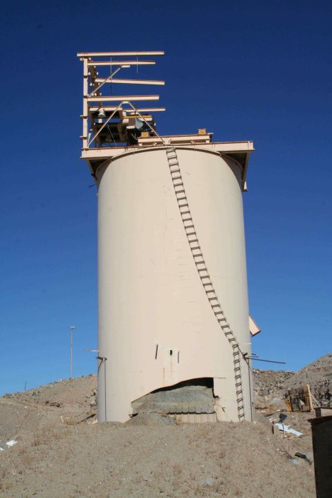1979 Ford Bronco - A tall, cylindrical industrial structure stands on a dusty, barren landscape under a bright blue sky.