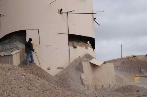 1979 Ford Bronco - A worker uses a torch to demolish a large industrial silo, with debris and gravel surrounding the structure.