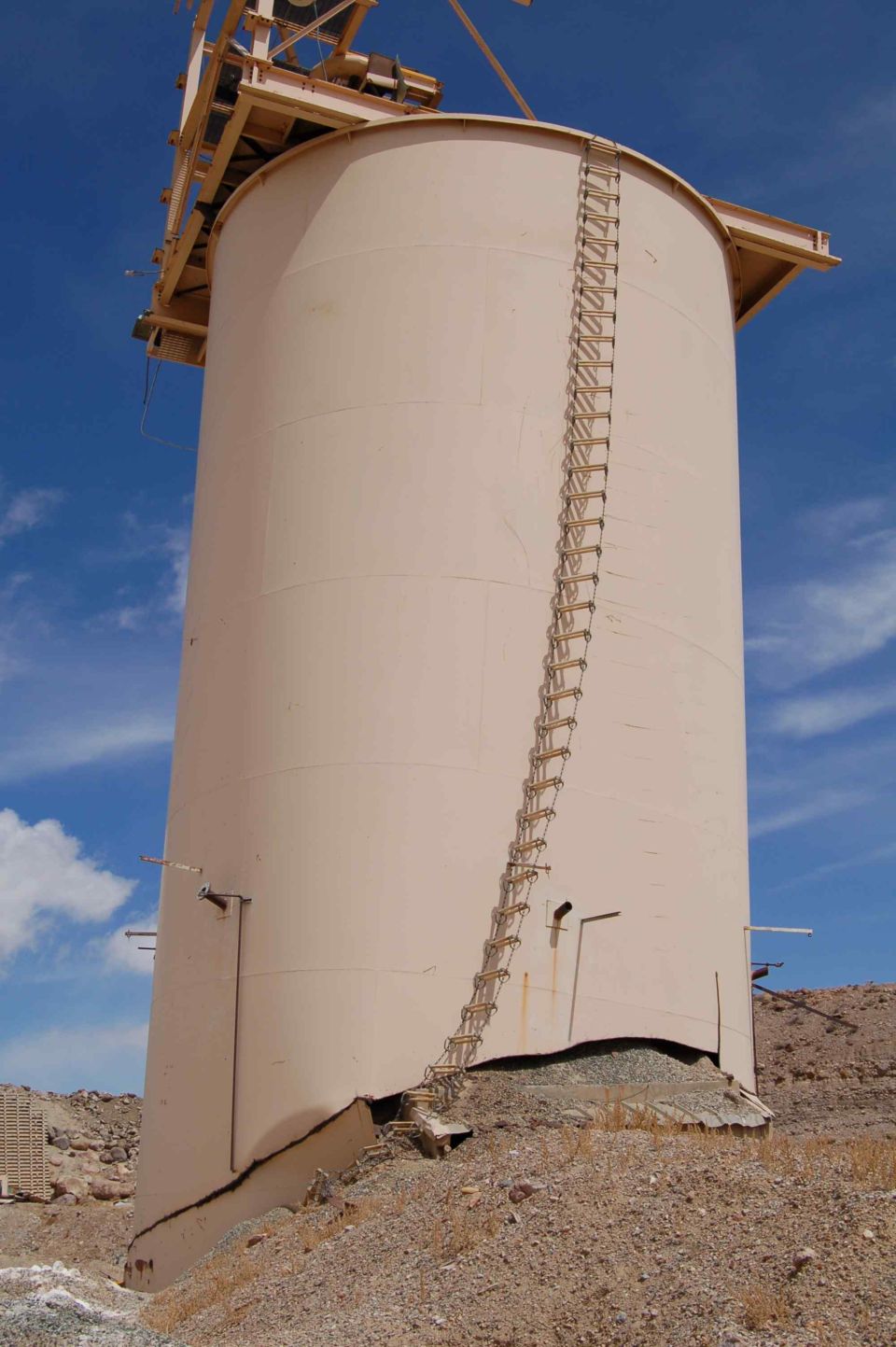 Damaged industrial silo with ladder against blue sky