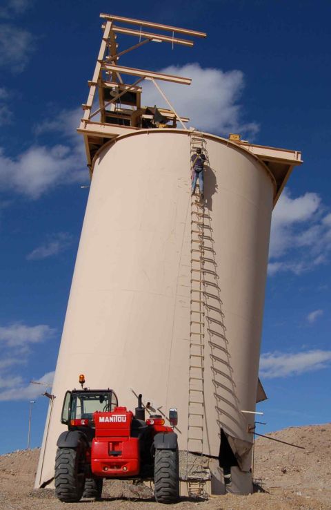 1979 Ford Bronco - Worker ascends a tall silo while a red Manitou telehandler is positioned at its base.
