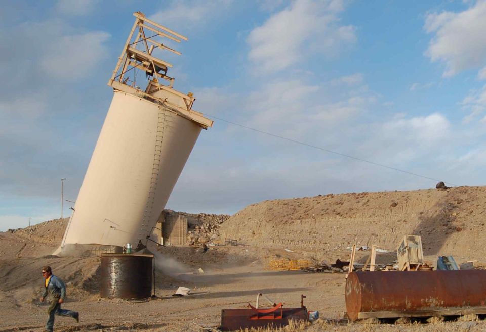 Person running from tilted silo in desert landscape
