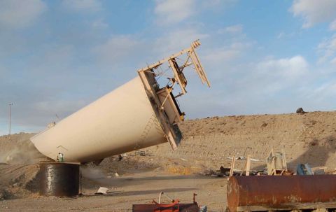 1979 Ford Bronco - A large industrial silo has toppled over in a dusty, arid environment, with debris scattered around.
