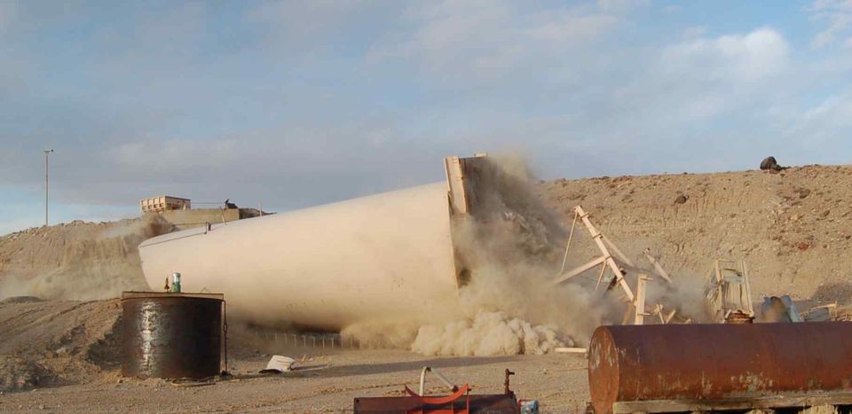 Large white cylindrical object falling in a dusty desert scene with construction equipment