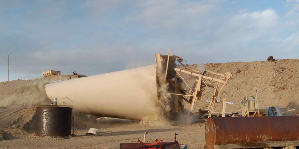 Large cylindrical object falling, kicking up dust, with wooden supports