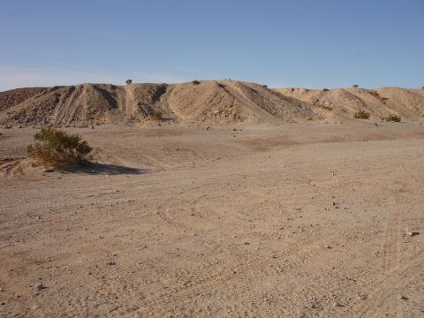 1996 Ford Bronco - A wide shot of a desert scene with tire tracks visible in the foreground and a barren hill in the background under a clear blue sky.
