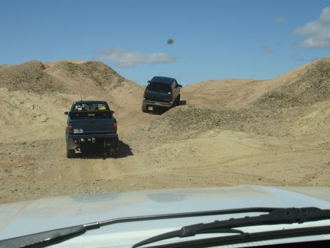 1996 Ford Bronco - Two trucks navigate a dusty, hilly terrain on a clear day.