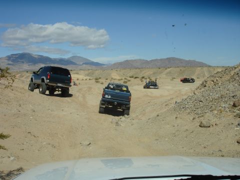 1996 Ford Bronco - Multiple vehicles traverse a desert landscape on a sunny day, with mountains in the background.