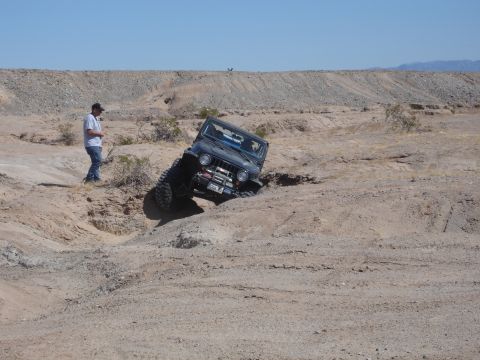 1996 Ford Bronco - A dark-colored Jeep Wrangler navigates a steep dirt incline in a dry, desert environment.