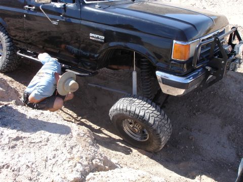 1996 Ford Bronco - A person works on the undercarriage of a black Ford Bronco with aftermarket suspension and tires.