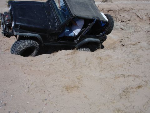 1996 Ford Bronco - A black Jeep Wrangler is stuck in the sand, with its tires partially buried.