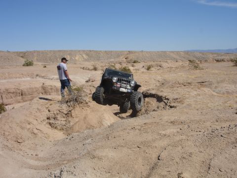 1996 Ford Bronco - A Jeep navigates a challenging off-road course in a dry, barren environment under a clear blue sky.