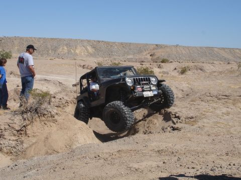 1996 Ford Bronco - A black Jeep Wrangler tackles a challenging off-road course in a desert environment.