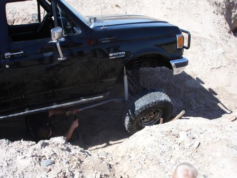 1996 Ford Bronco - A black Ford Bronco with a lifted suspension is stuck in the dirt, with a person working on it from underneath.