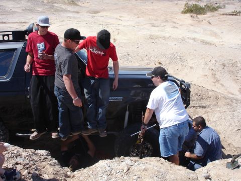 1996 Ford Bronco - A group of friends attempts to free a stuck Ford Bronco from a deep pit in a sandy, arid landscape.