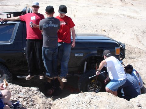 1996 Ford Bronco - A group of people gather around a black 1996 Ford Bronco that appears to be stuck in a dirt pit, with some attempting to work on the front…