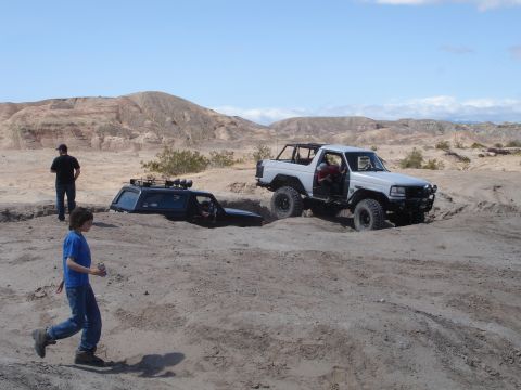1996 Ford Bronco - Two off-road vehicles are stuck in a sandy ditch in a desert landscape under a clear blue sky.