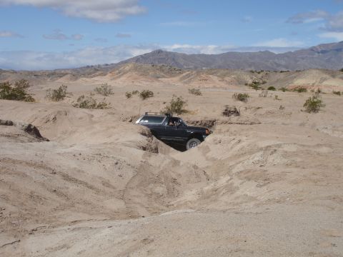 1996 Ford Bronco - A 1996 Ford Bronco drives through a challenging sandy terrain with mountains in the background.