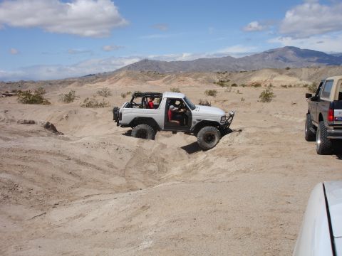 1996 Ford Bronco - Two Broncos off-roading in a desert landscape under a partly cloudy sky.