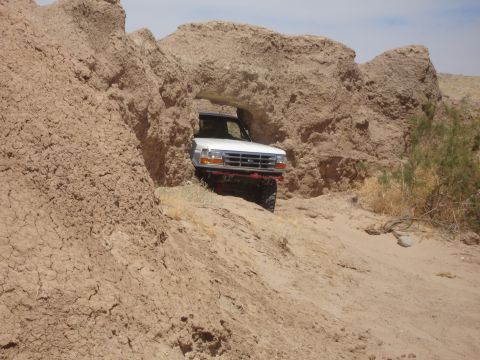 1996 Ford Bronco - A white 1996 Ford Bronco navigates through a natural rock archway in a desert environment.