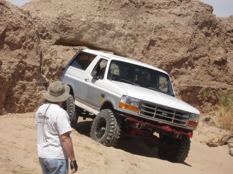 1996 Ford Bronco - A white Ford Bronco navigates a rocky, sandy terrain with a person observing the off-road adventure.