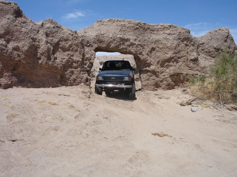 1996 Ford Bronco - A dark blue SUV navigates through a sandy path under a large rock formation on a sunny day.