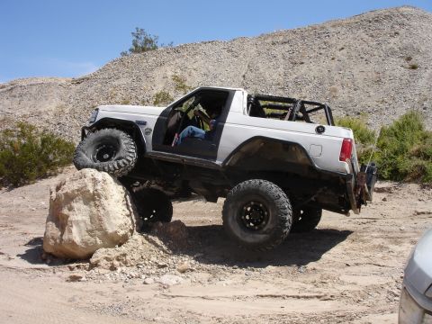 1996 Ford Bronco - This modified SUV is navigating a challenging off-road obstacle on a sunny day.