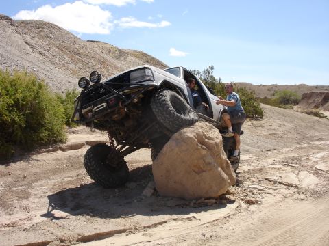1996 Ford Bronco - A modified SUV navigates a challenging rocky terrain, with two people inside and one assisting from the exterior.