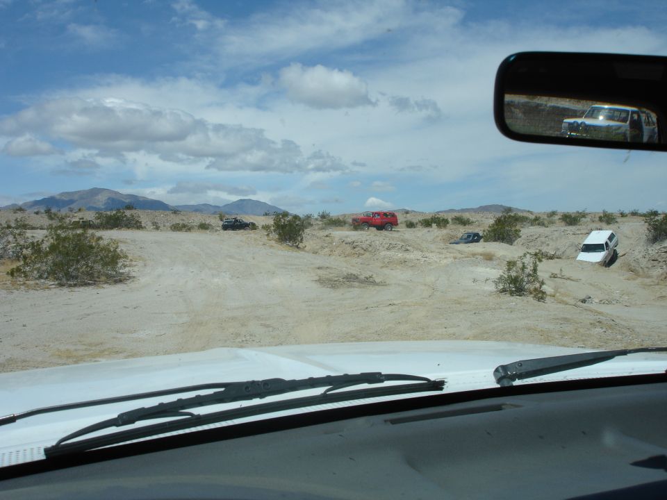Desert scene with several SUVs and trucks off-roading, view from inside a vehicle