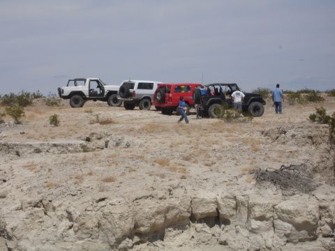 1996 Ford Bronco - Group of off-road vehicles gathered on a rocky desert terrain under a cloudy sky.