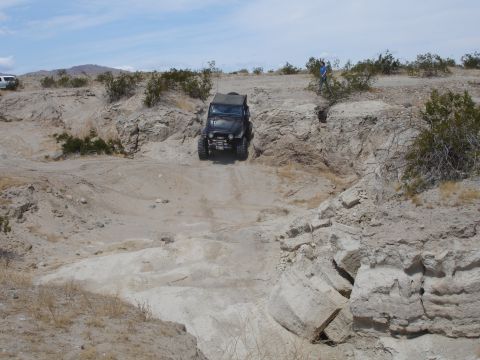 1996 Ford Bronco - A Jeep navigates a challenging off-road course with steep inclines and rocky terrain under a bright sky.